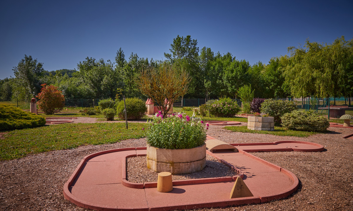 At Le Chêne Vert, there is a mini-golf course that includes concrete walkways and garden beds encircled by vibrant foliage and trees.