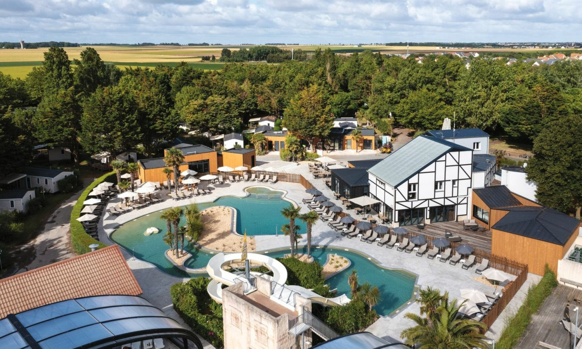 A resort with a swimming pool and water slide surrounded by trees and cabins at La Côte de Nacre