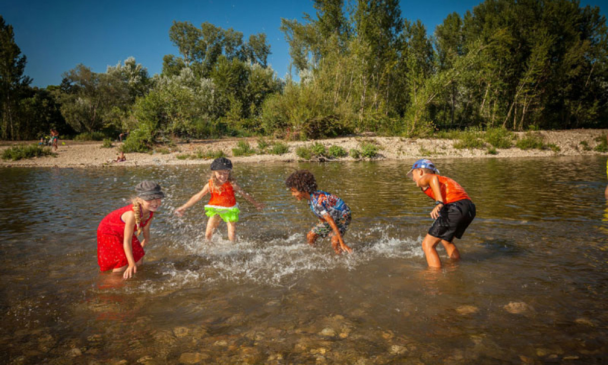 At La Sousta, kids are frolicking and splashing in a shallow stream, encircled by vibrant foliage and stones.