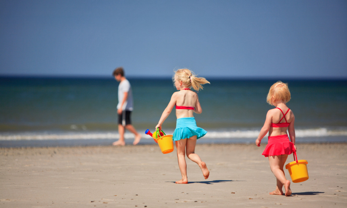 At Dancamps Nordsø, two kids are running on a sandy shore with yellow pails, accompanied by the sound of ocean waves in the background.