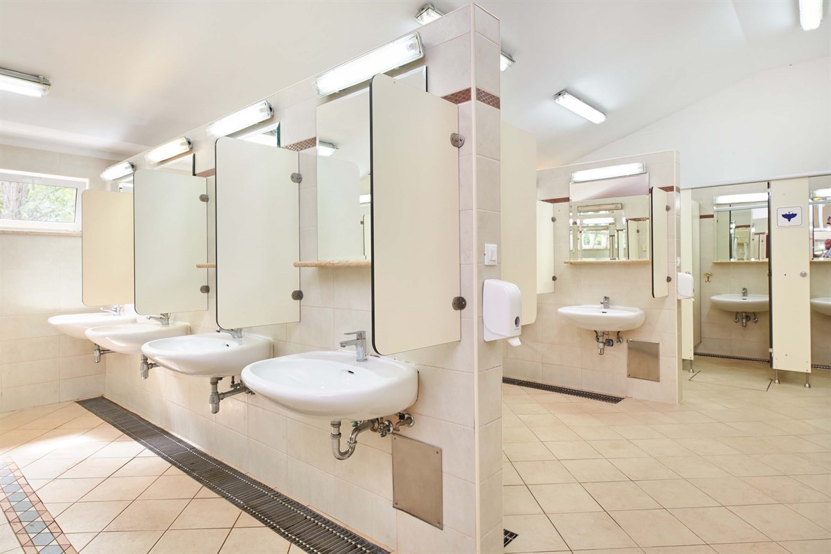 At Naturist Ulika, there are sinks and mirrors divided by partitions in a tiled restroom.