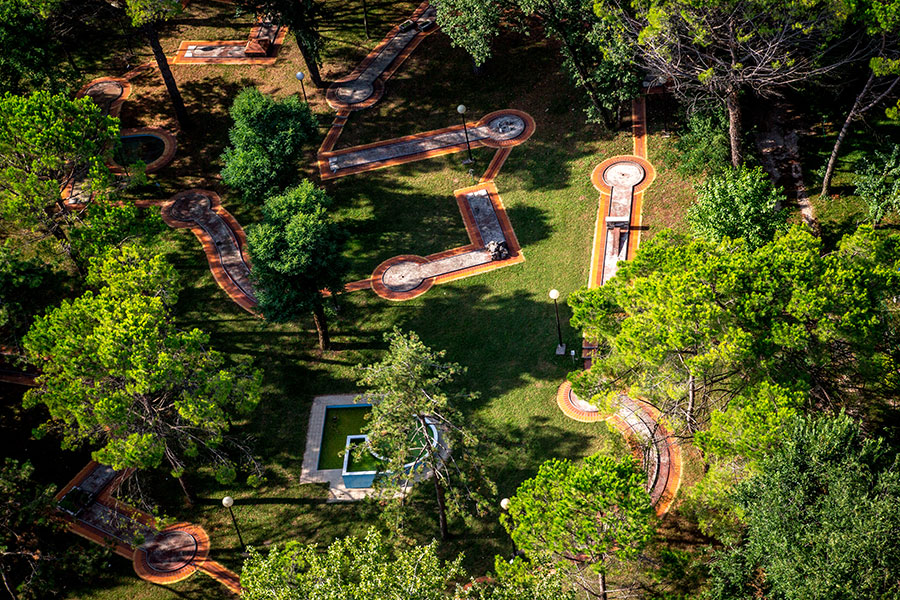 Mini-golf course viewed from above, featuring winding paths and surrounded by tall, lush green trees at Belvedere Pineta