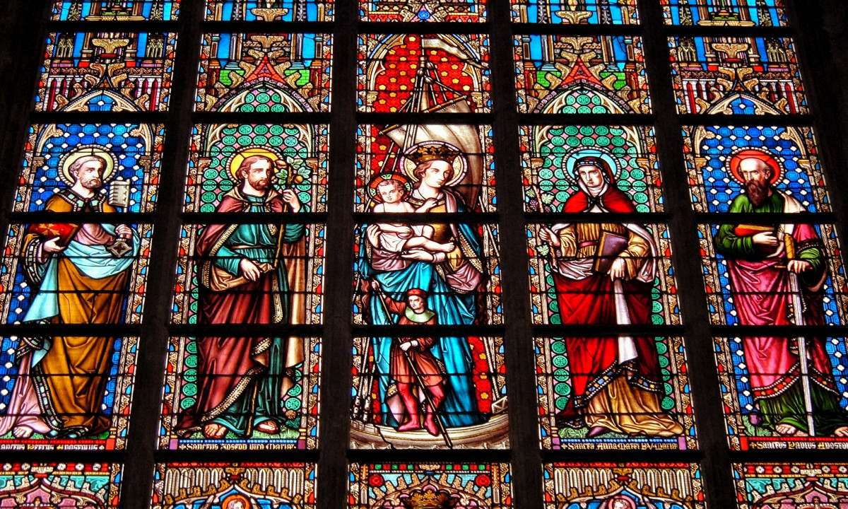 At Urban Gardens Gent, a lively stained glass window illustrates religious figures in vivid garments, positioned against a detailed, elaborate architectural backdrop.