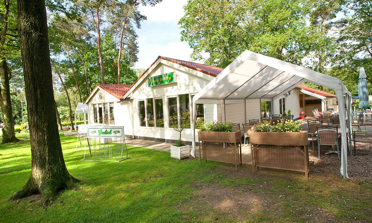 White building with a red roof and an open-air dining area, surrounded by trees and grass at de Wrange