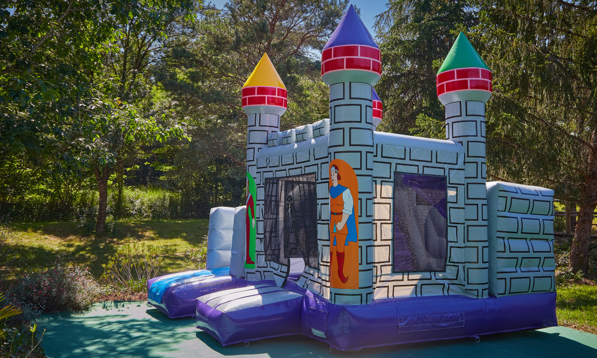 At Le Chêne Vert, an inflatable castle bouncer stands unused, encircled by vibrant trees and greenery.