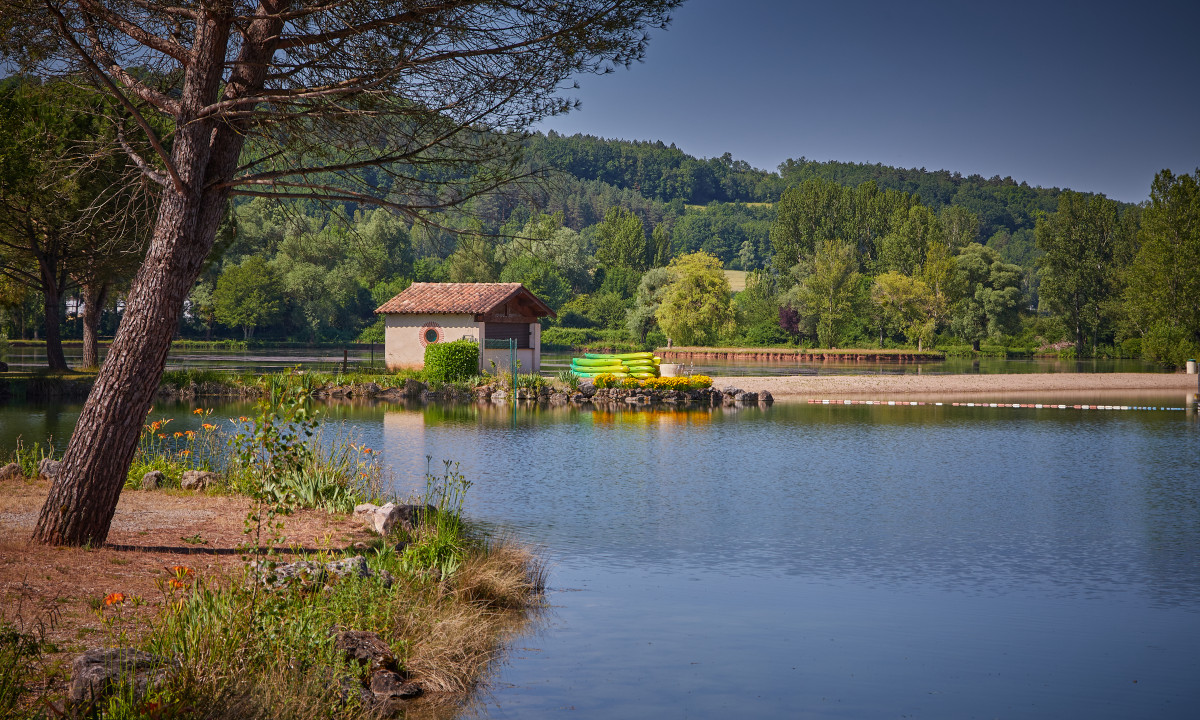 At Le Chêne Vert, a tranquil lake features a boathouse encircled by vibrant foliage and neatly arranged kayaks.