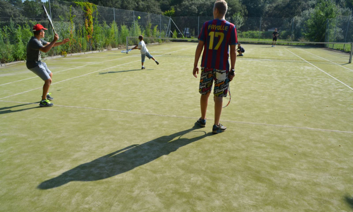 At La Sousta, individuals are engaged in doubles tennis on a neglected court encircled by trees.