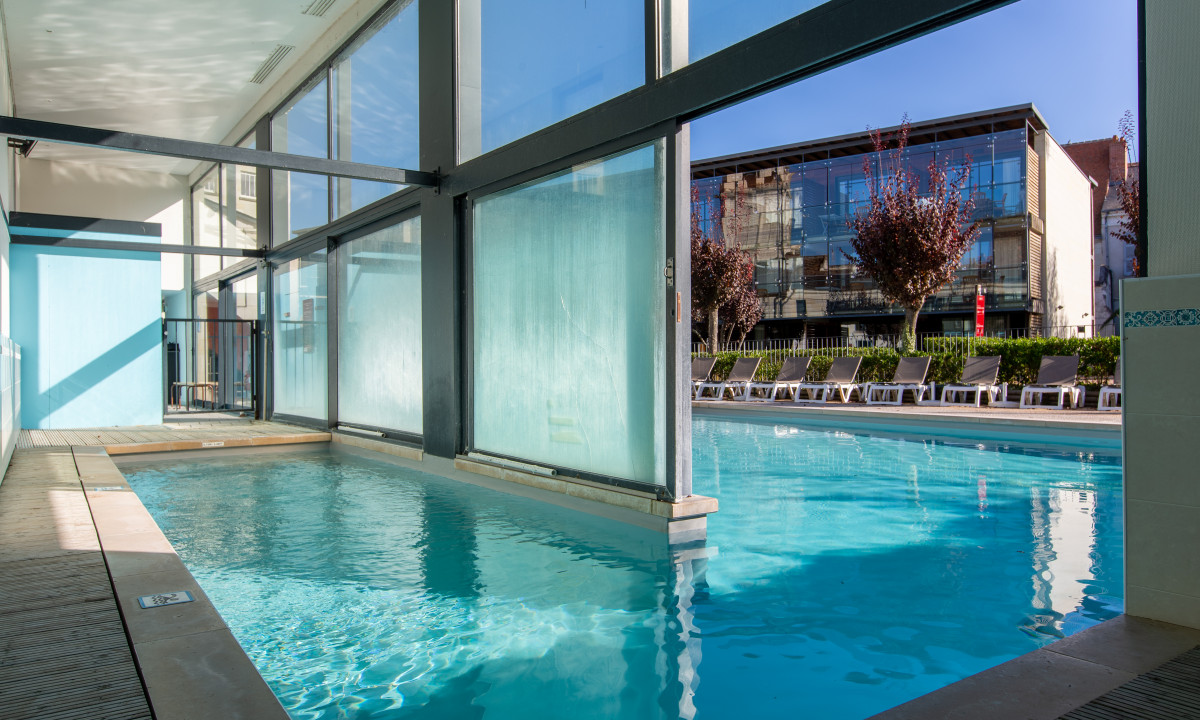 Indoor pool connects to outdoor pool through glass wall in a modern building at Le Moulin des Cordeliers