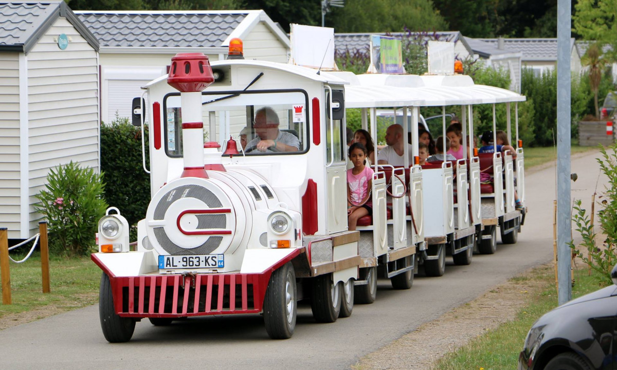 At Le Domaine de Léveno, a white and red tourist train carries visitors along a path in a campground featuring mobile homes.