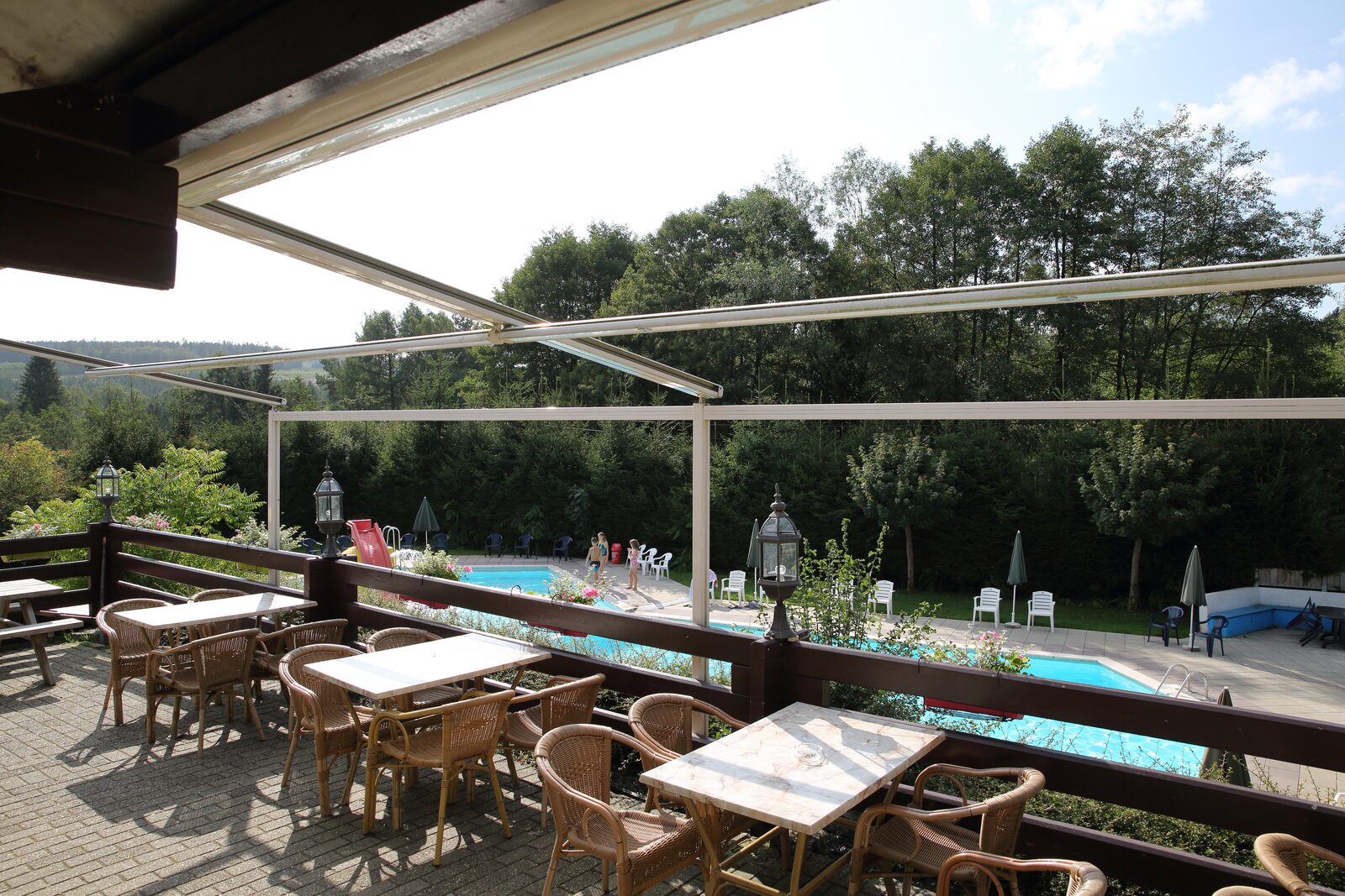 At Petite Suisse, tables and chairs are set up on a patio that overlooks a swimming pool encircled by trees.