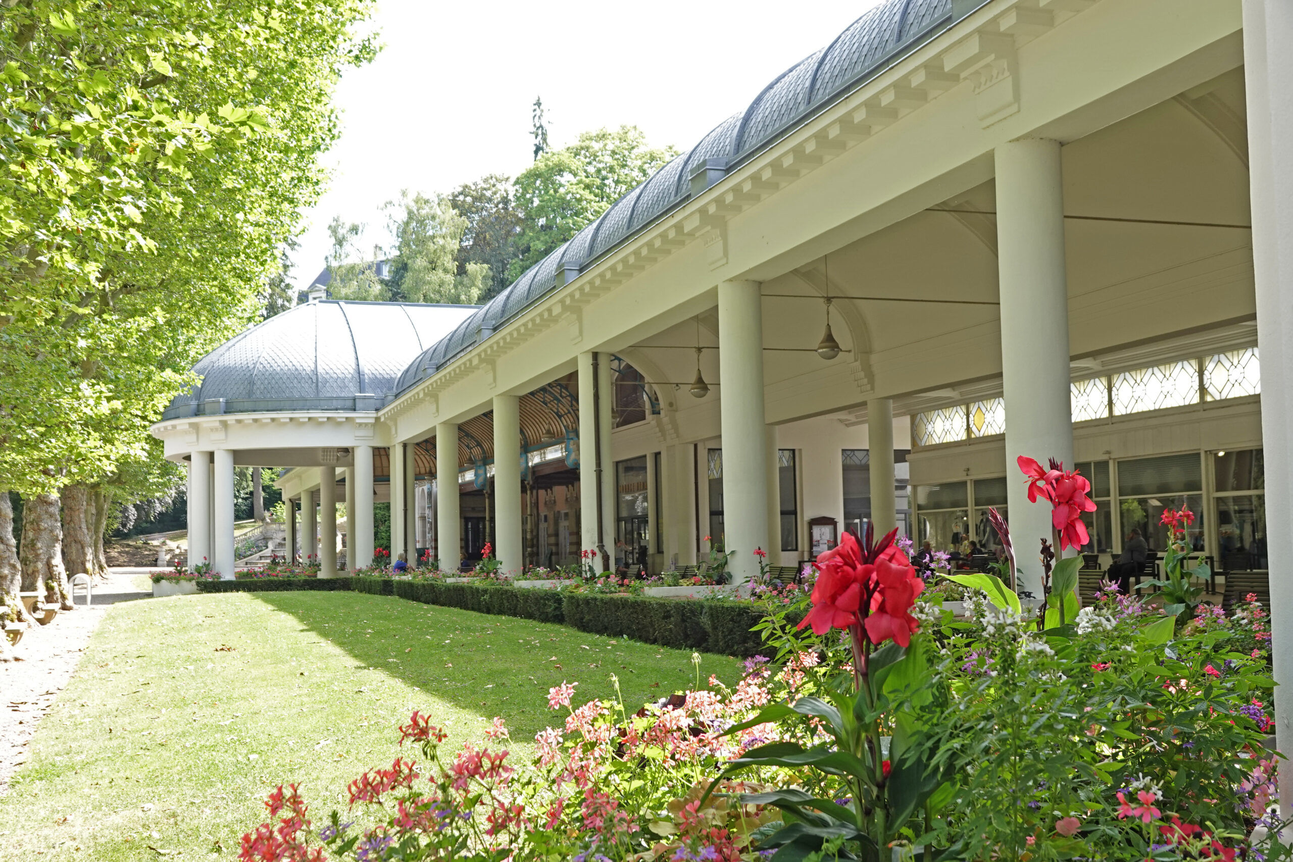 Building with a curved roof and columns surrounded by lush gardens, path, and trees at Seasonova Vittel