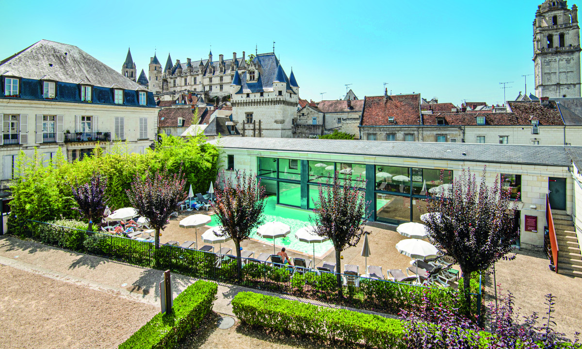 Sunbathers relaxing by a pool with greenish water, surrounded by trees and historic buildings at Le Moulin des Cordeliers