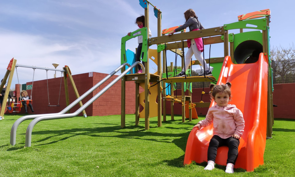 Children playing on playground equipment with swings and slides on a grassy play area at Resort Els Pins
