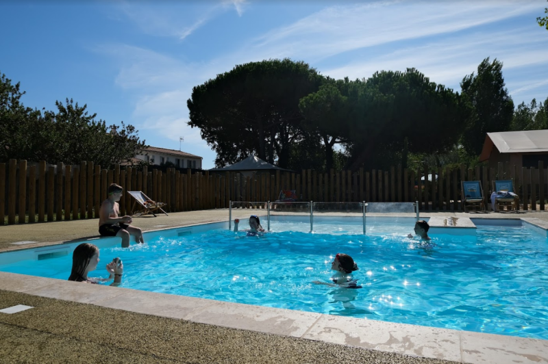 Children swimming and playing in a small outdoor pool surrounded by trees and lounge chairs at Seasonova Ile de Ré
