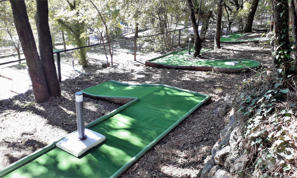At La Clémentine, a miniature golf course meanders through a forested region, with sunlight streaming through the trees.