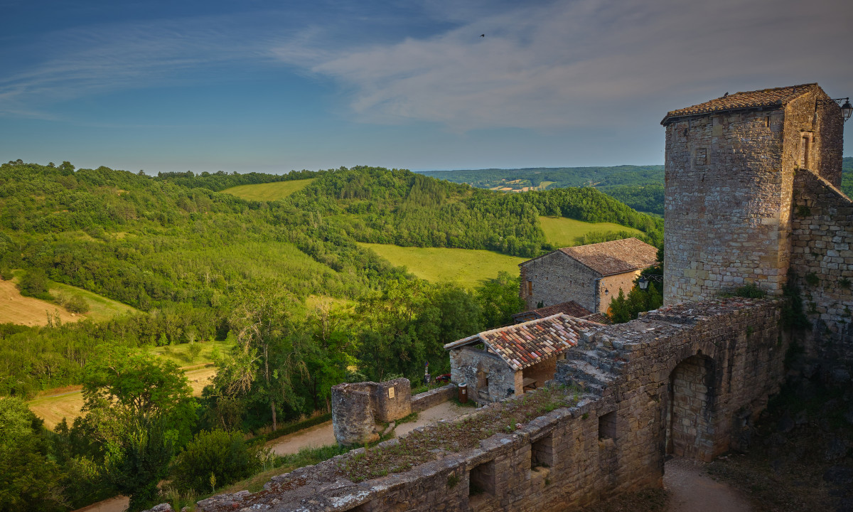 At Le Chêne Vert, a rocky stronghold gazes over verdant, rolling hills beneath a clear sky.