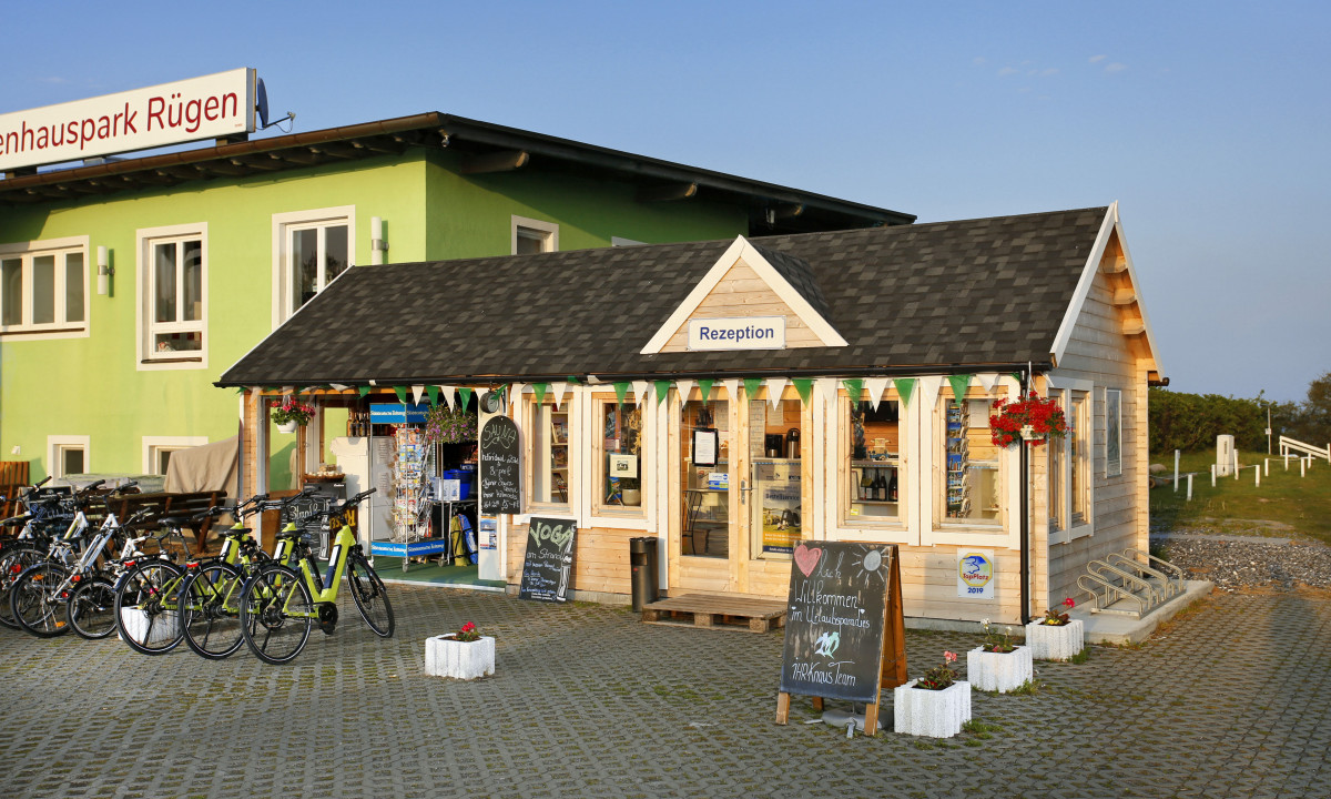 At KNAUS Campingpark Rügen, a quaint wooden structure functions as a reception area, with bicycles stationed outside, adjacent to a green building.