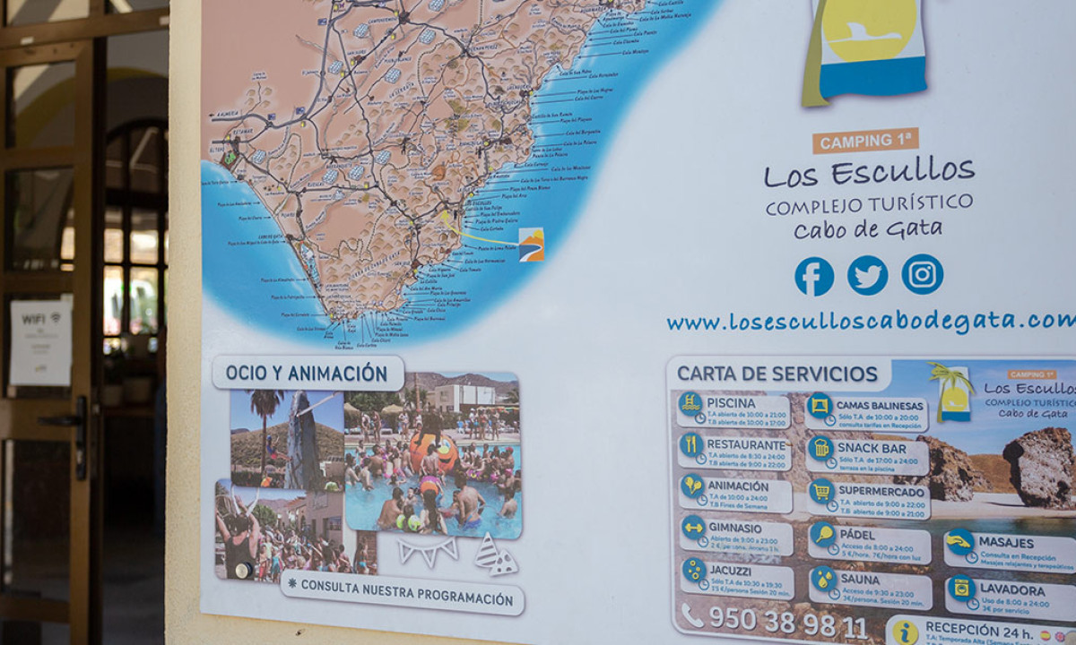 At Camping Los Escullos, a poster on the wall displays a map and images of recreational activities, along with service information.