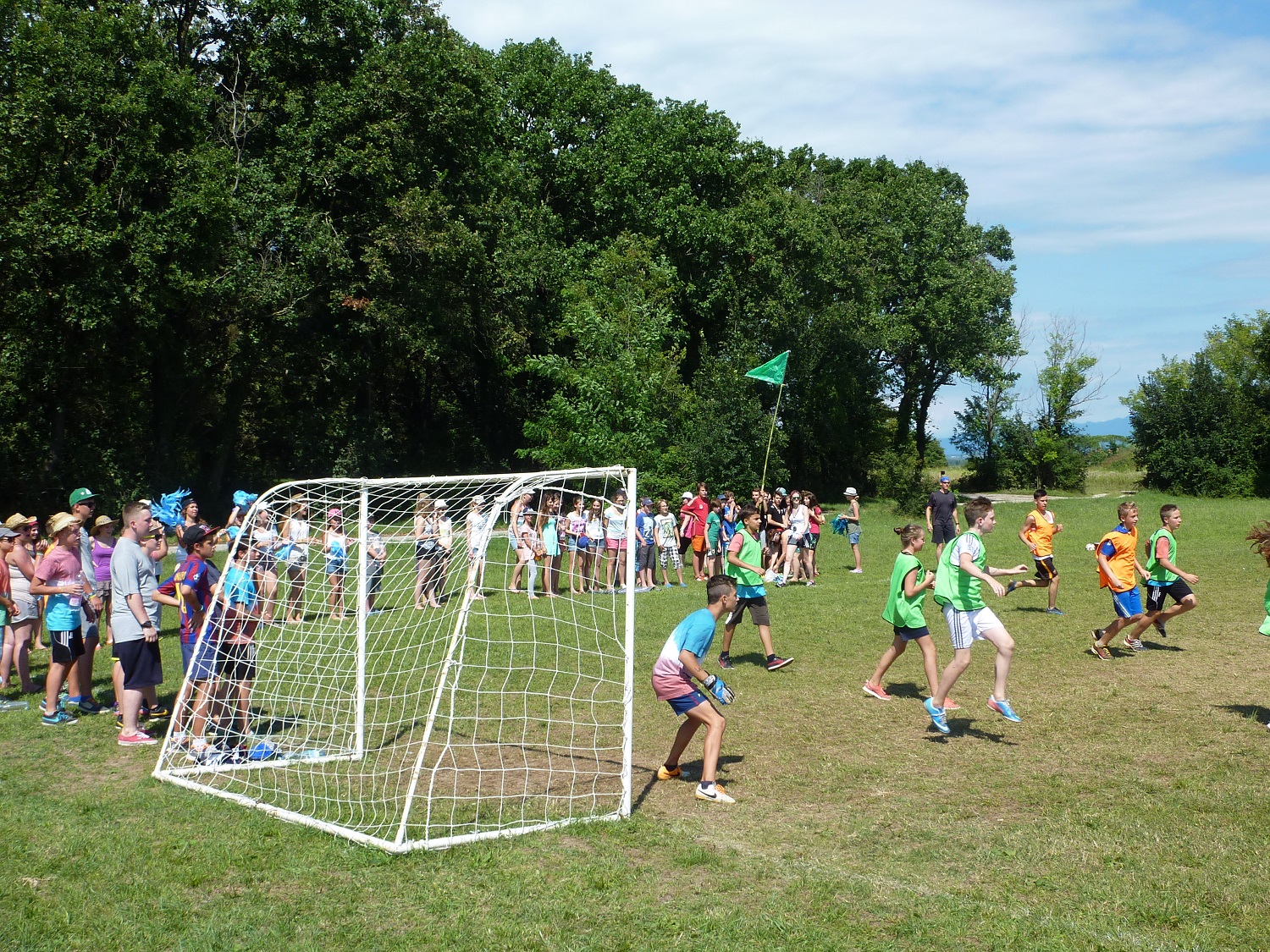 Children playing soccer in a field while spectators watch, surrounded by trees and a sunny sky at Belvedere Pineta