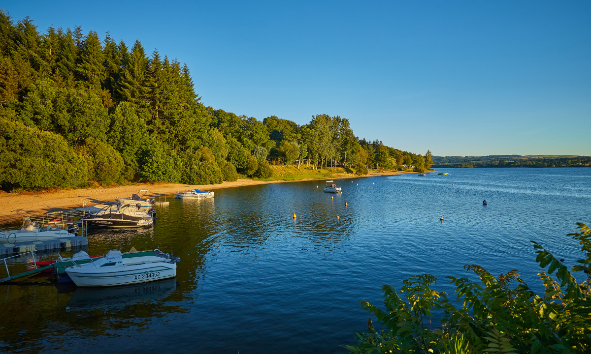 At Terrasses du Lac, vessels drift on a tranquil lake adjacent to a sandy beach encircled by thick woodland.