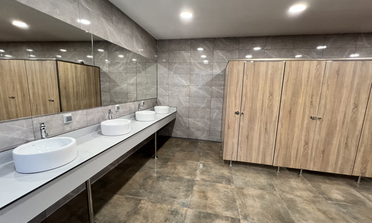 Sinks on a long counter with mirrors, next to wooden bathroom stalls, in a tiled restroom at Resort Els Pins