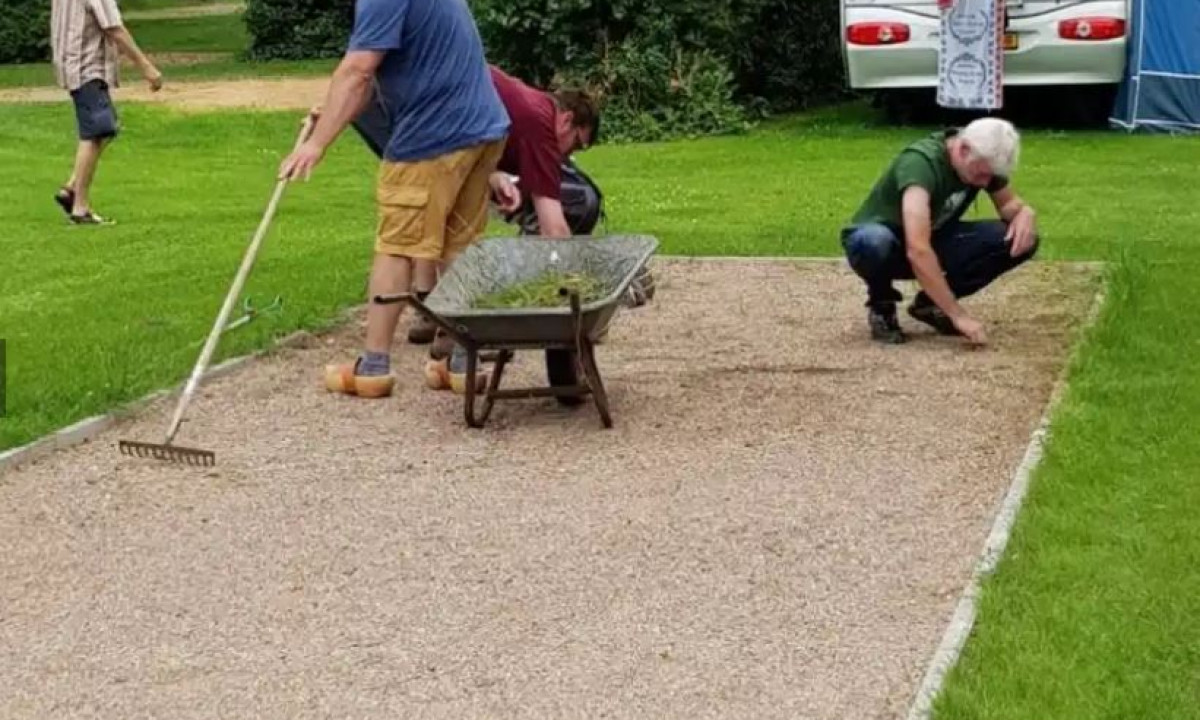 At Elbeling, individuals are leveling gravel and removing weeds at the campsite, with a wheelbarrow close by.