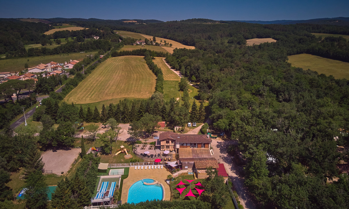 At Le Chêne Vert, an overhead perspective showcases a camping area with a swimming pool, water slides, and structures surrounded by meadows and woodlands.