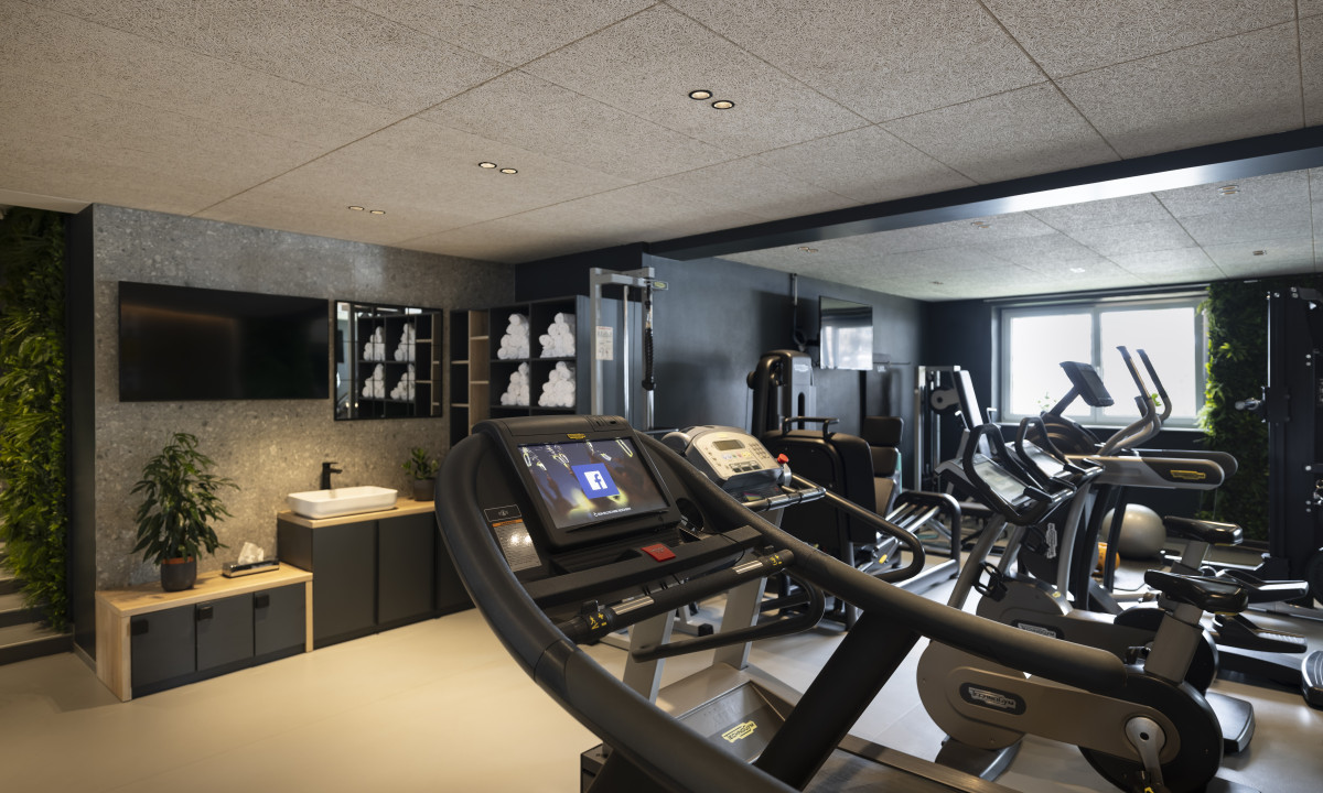 Exercise equipment sits unused in a modern gym with plants and a television on the wall at Kesselspitze Valamar Collection Hotel