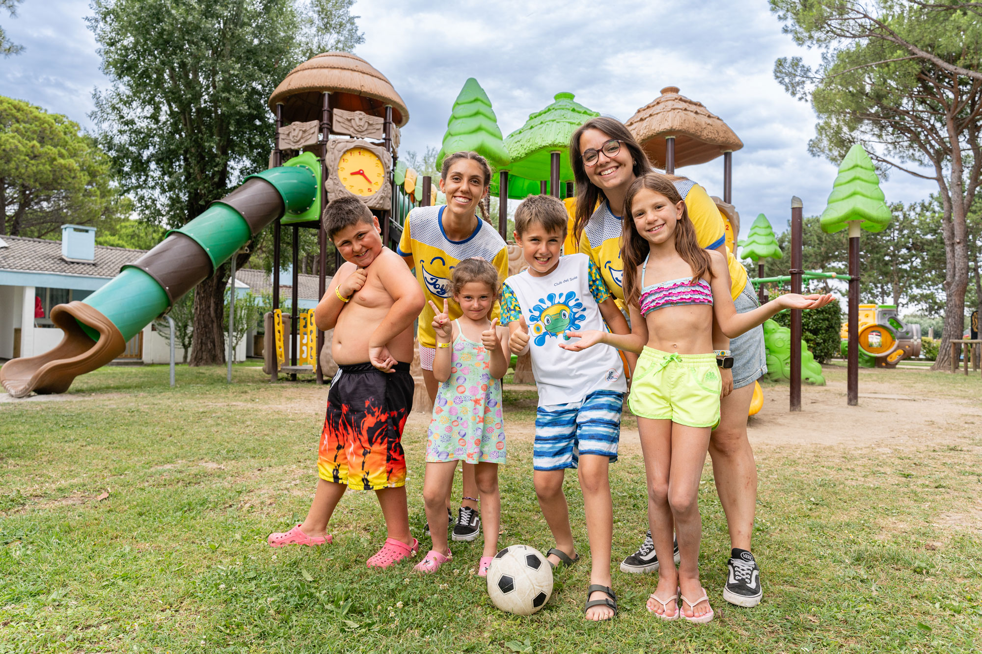 Group of smiling children and adults posing together in front of a colorful playground at Marina Julia Family Camping Village