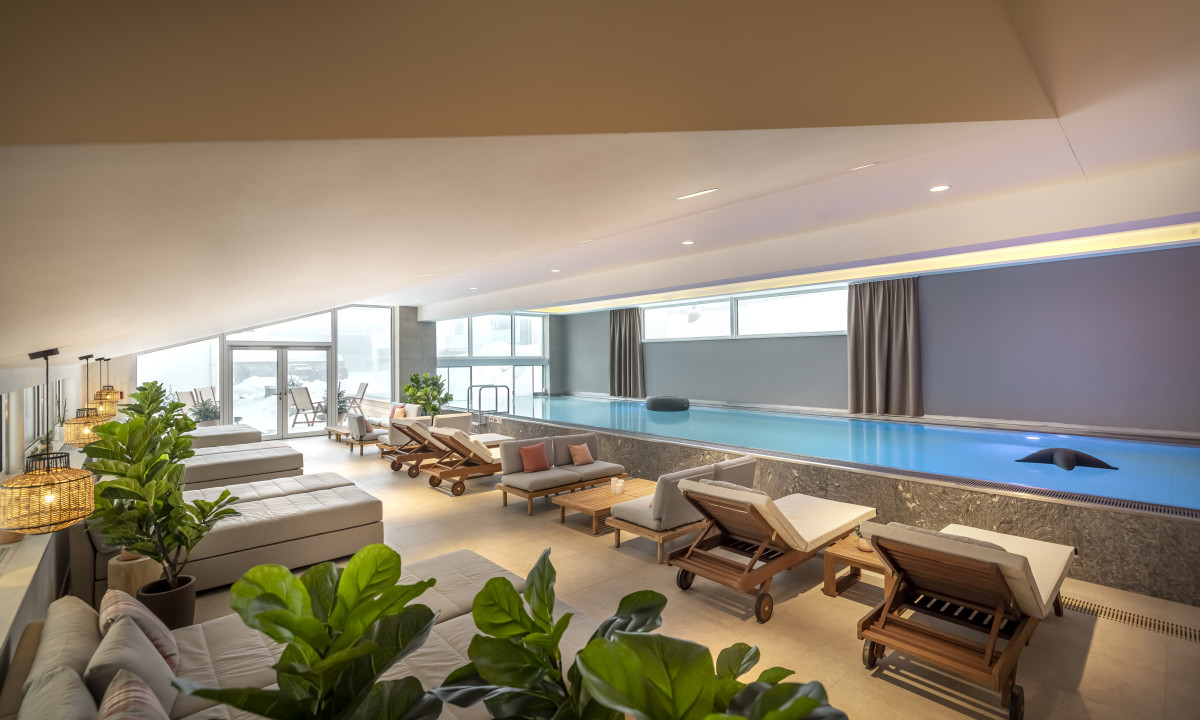 Indoor pool with lounge chairs beside, surrounded by potted plants in a modern, well-lit setting at Valamar Obertauern Hotel