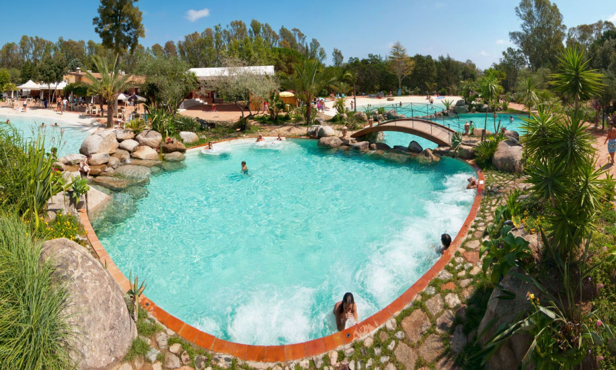 At Ultima Spiaggia, individuals are swimming in a pool encircled by stones, greenery, and a petite bridge.