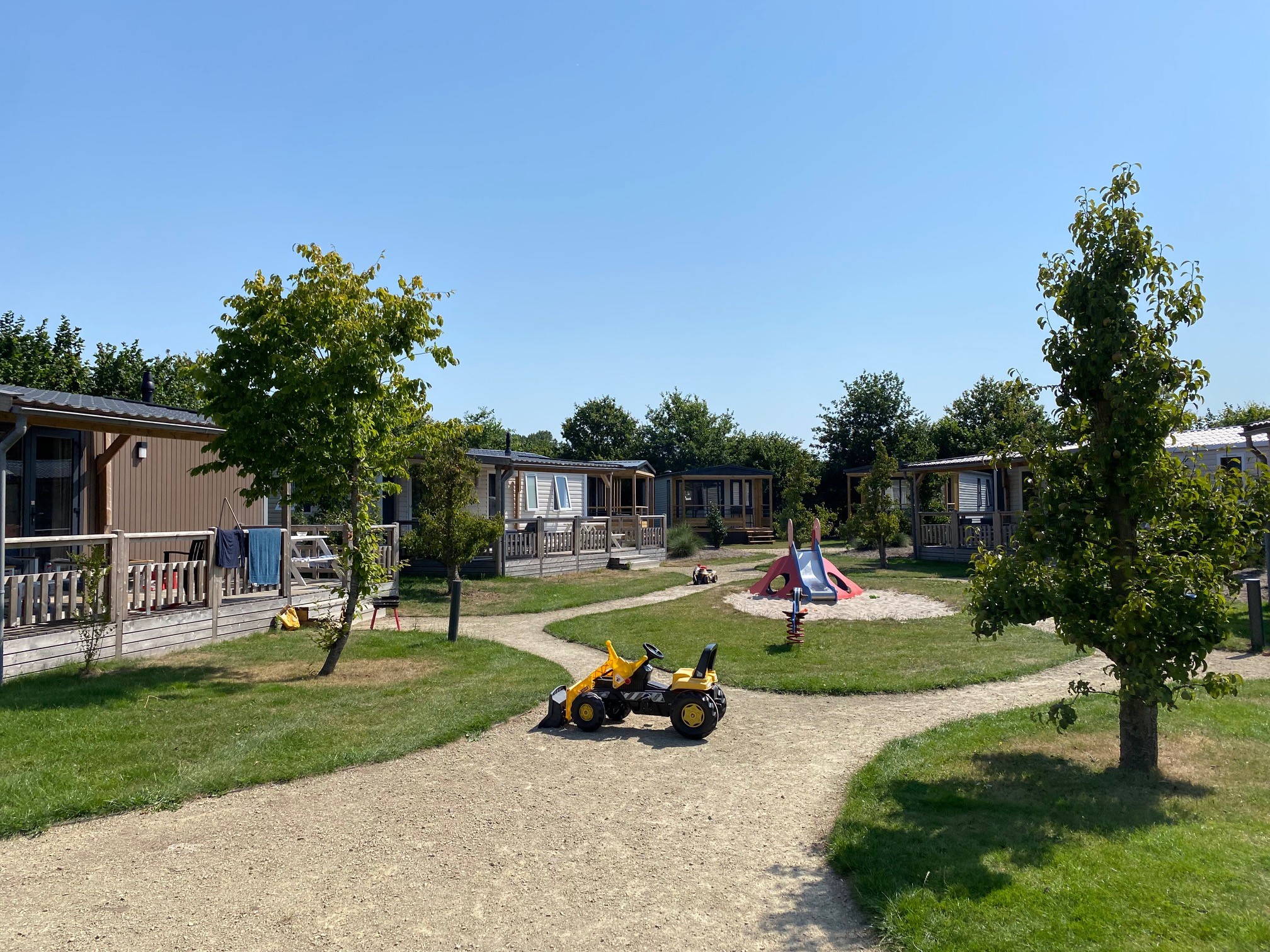 At de Vinkenkamp, there is a children's play area featuring toys and a slide, encircled by trees and cabins.