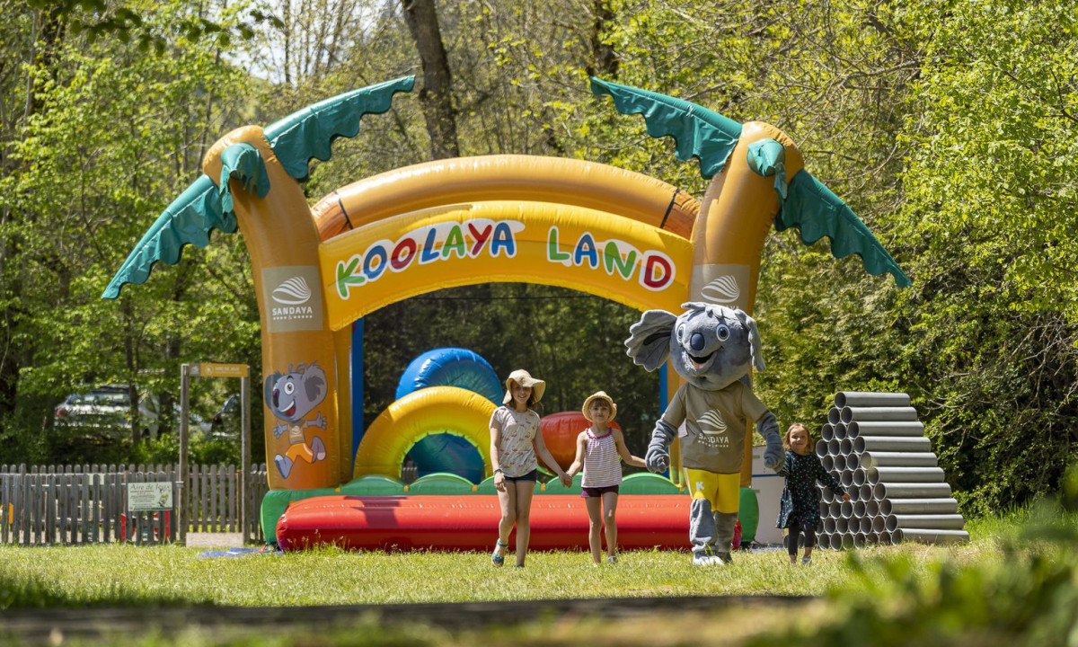 Inflatable archway with kids and a mascot walking in a grassy area near a forest at La Ribeyre