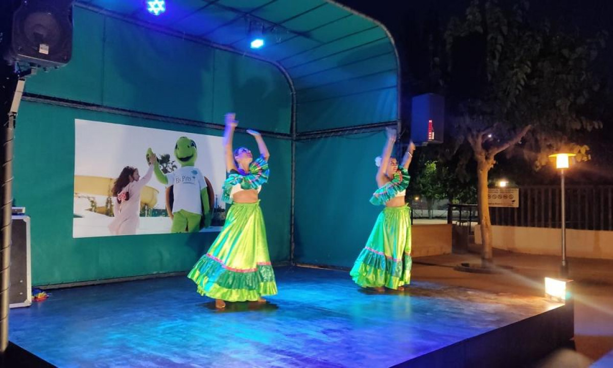 Two women perform traditional dance on a small, lit stage at night, surrounded by trees at Resort Els Pins