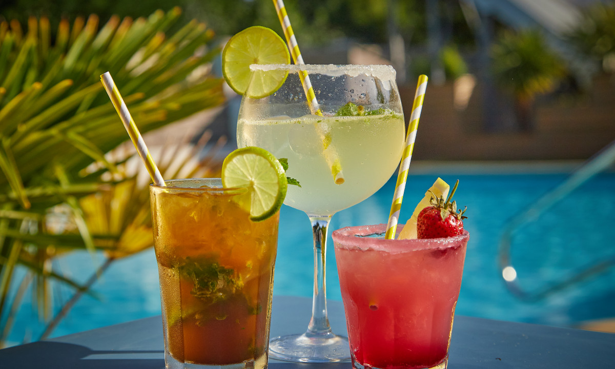 At Le Chêne Vert, beverages rest on a table by the pool, each adorned with fruit wedges and decorative straws.