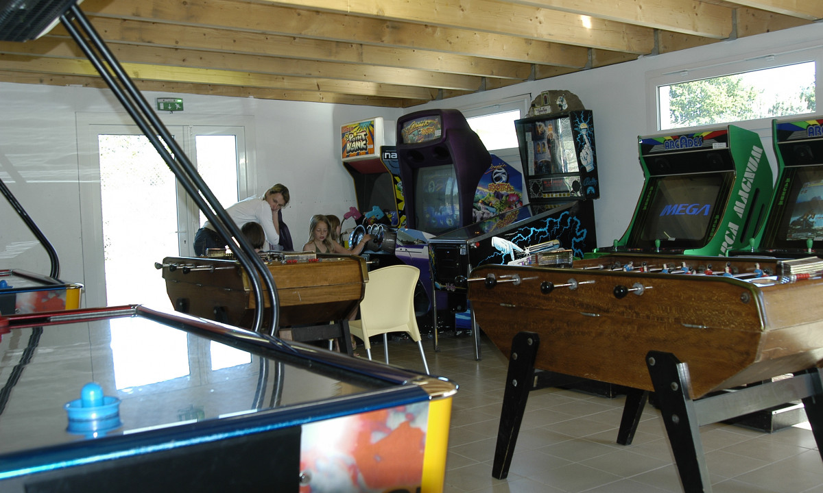At Le Domaine de Léveno, young people are enjoying arcade games and foosball in a game room with a wooden ceiling.