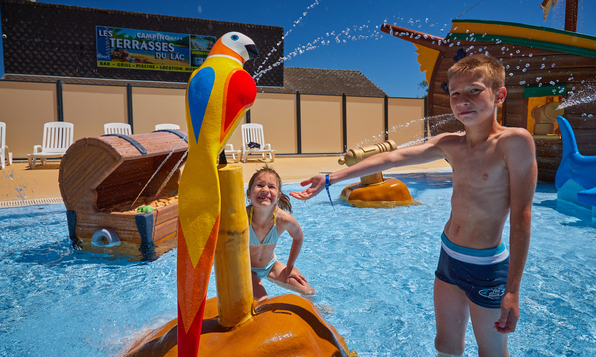 At Terrasses du Lac, two kids are enjoying themselves in a splash pad with water spraying elements and outdoor seating.