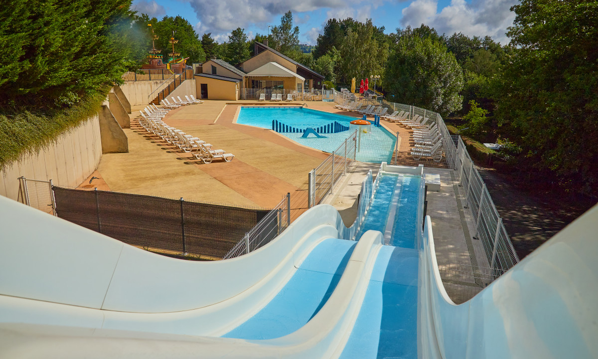 At Terrasses du Lac, water slides spiral into a spacious swimming pool encircled by lounge chairs and trees.