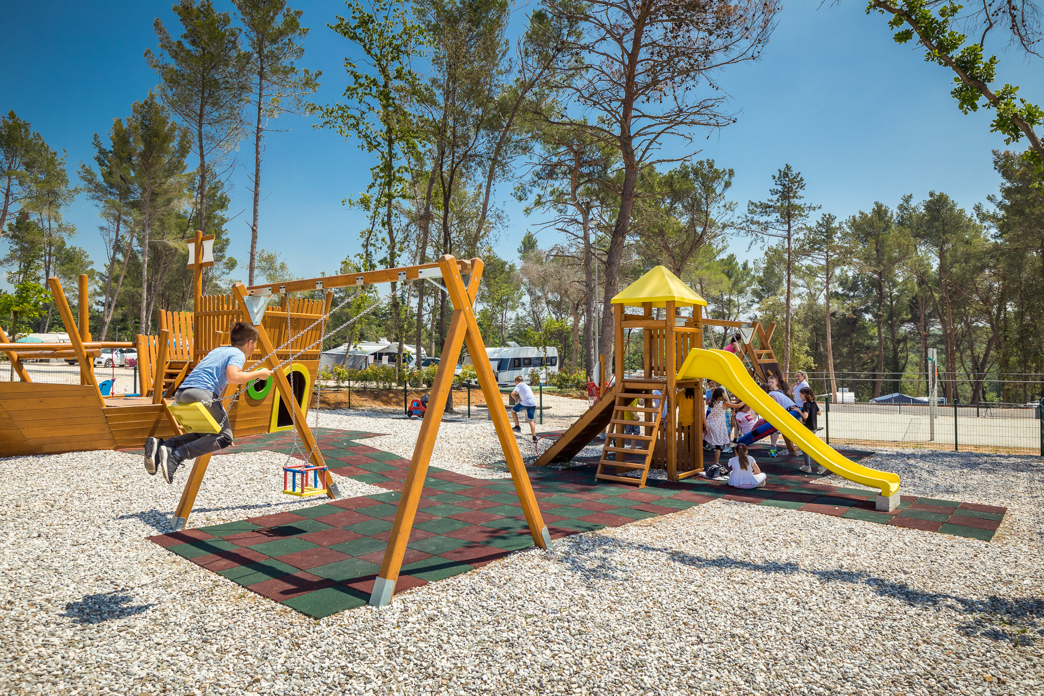 Children playing on a playground with swings and a slide, surrounded by tall trees at Santa Marina Boutique
