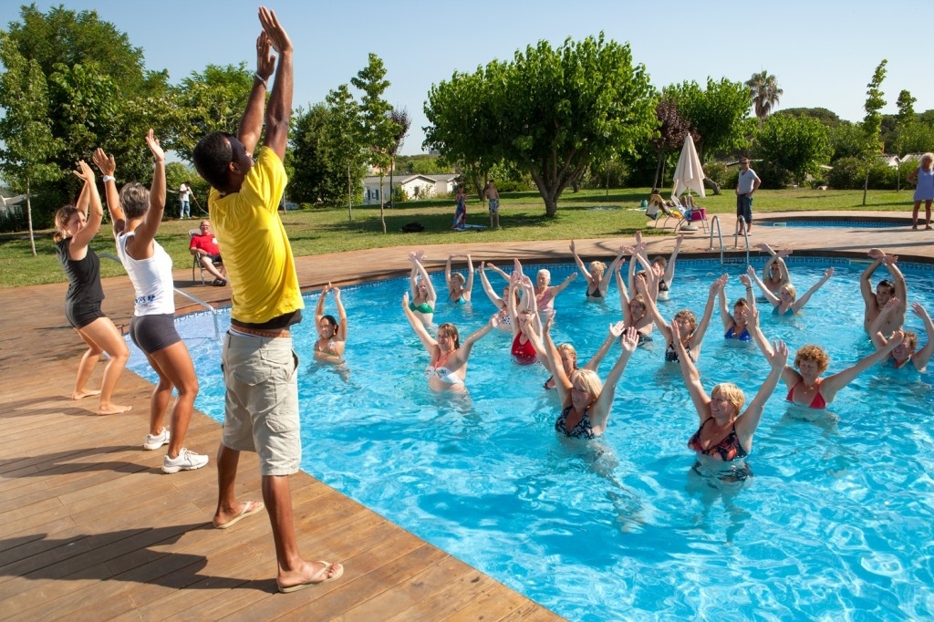 People performing a group water aerobics class in a pool, led by instructors on the poolside at El Pinar