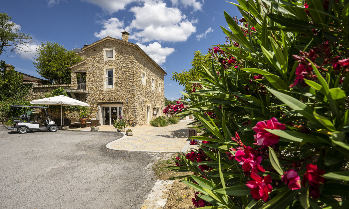 Stone building with a golf cart parked outside, surrounded by greenery and pink flowers at Domaine de Sévenier