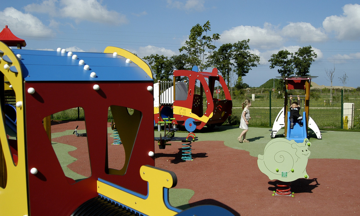 At Le Domaine de Léveno, kids are enjoying themselves on vibrant play structures outside beneath a clear blue sky.