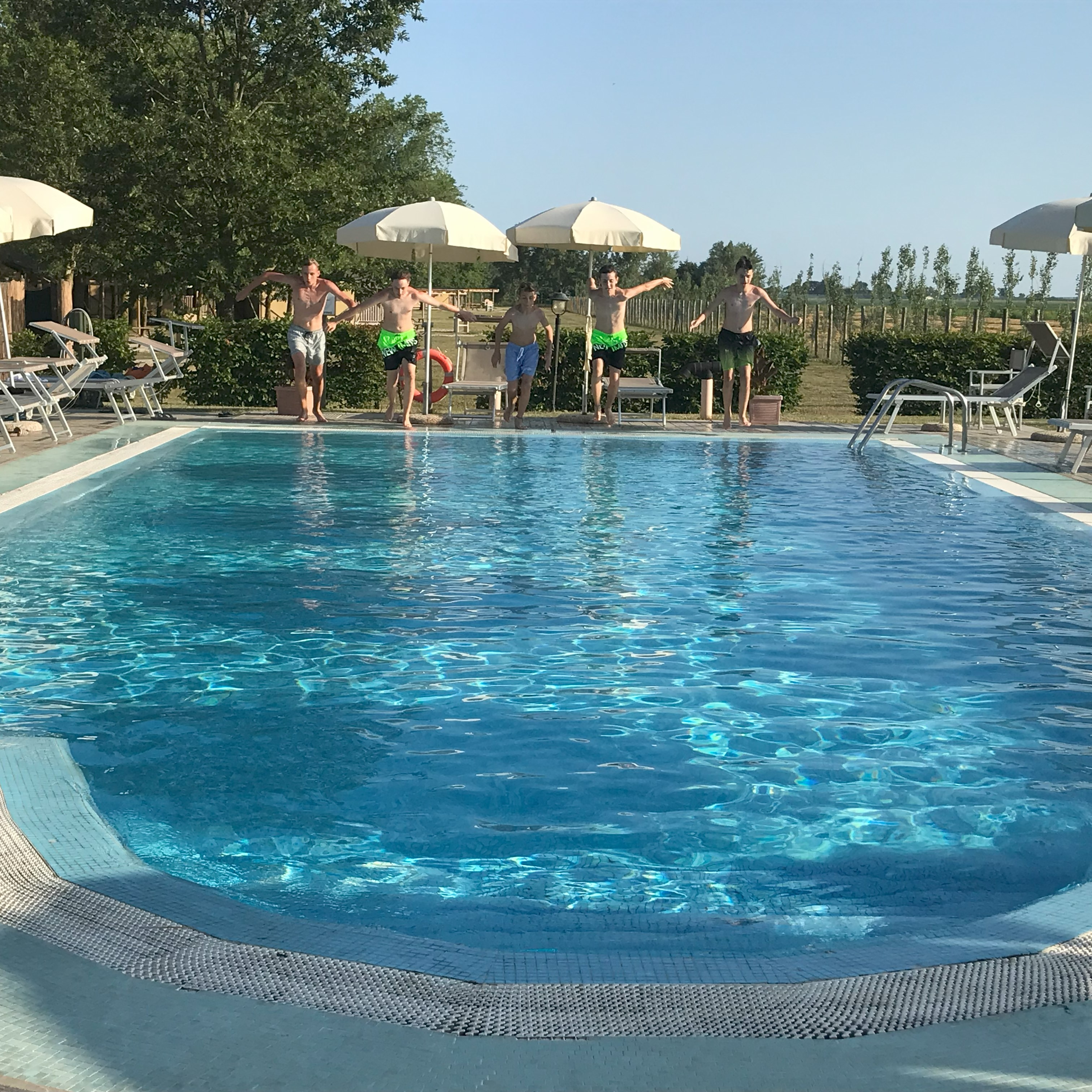 Five people about to jump into a swimming pool, surrounded by lounge chairs and umbrellas at Agriturismo Tenuta Regina