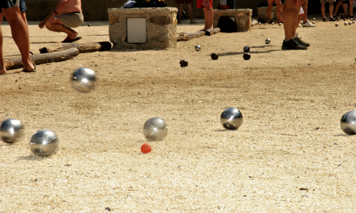 At La Clémentine, metal spheres are rolling on gravel while individuals nearby are engaged in an outdoor boules game.