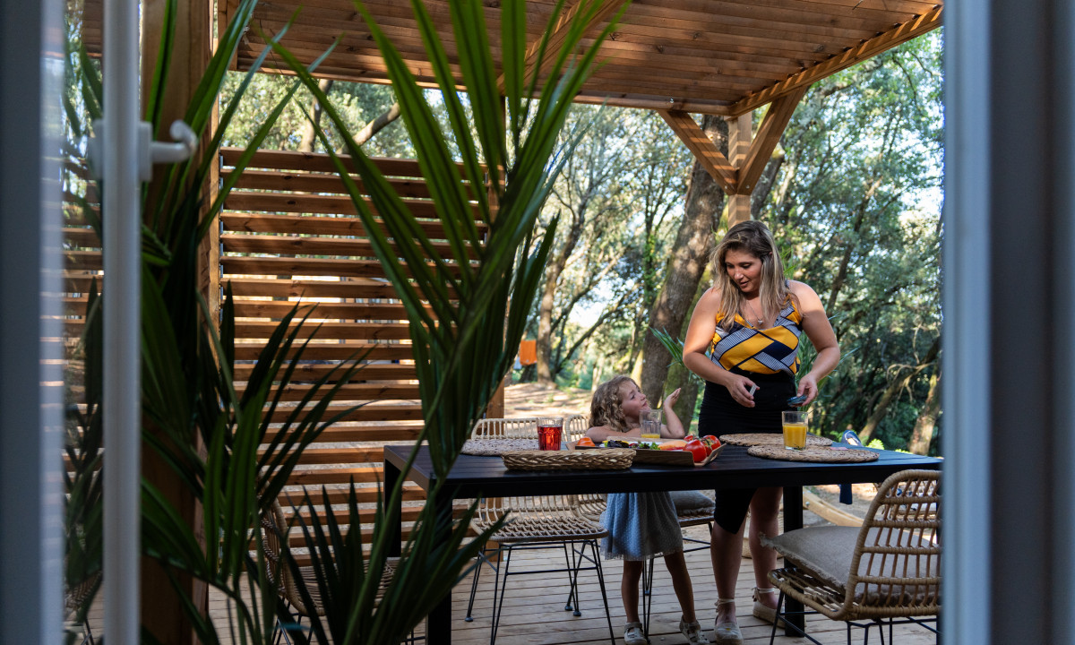 At La Clémentine, a woman and a child arranged a table on a timber deck encircled by trees.