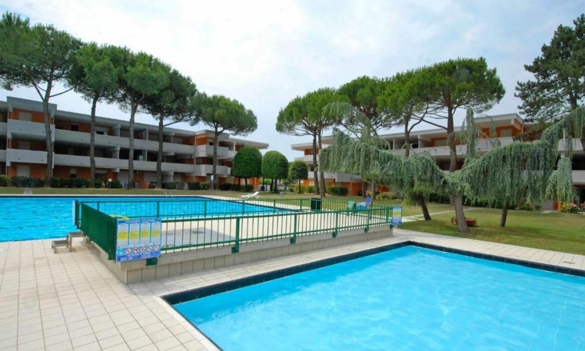 Swimming pools with blue water amid green trees and multi-story buildings in a landscaped area at Solarium