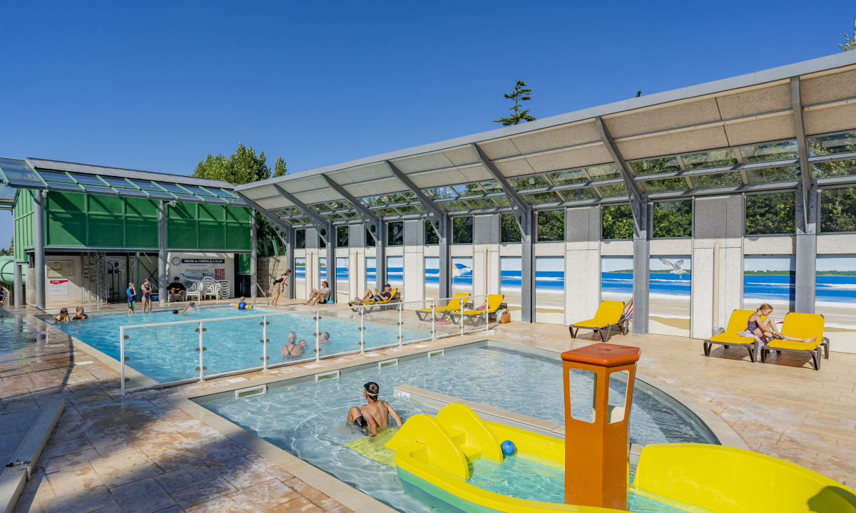 At De la Plage, individuals are relishing a swimming pool with deck chairs beneath a partially open ceiling, encircled by a beach-themed mural.