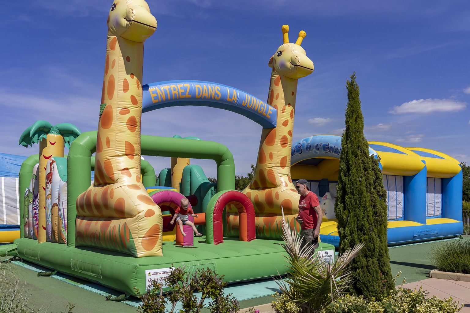 At Le Carbonnier, a jungle-themed inflatable bounce house is filled with children playing, encircled by trees and lush greenery.