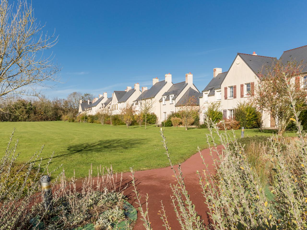 Row of white houses with gray roofs, surrounded by lush green lawns and shrubs, under a clear blue sky at Le Green Beach