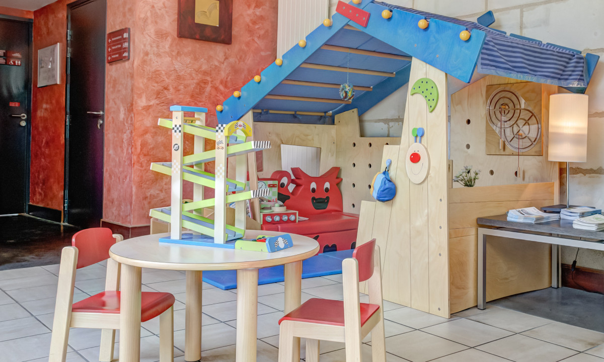 Children's play area with a wooden table, chairs, and a toy structure in a brightly colored indoor setting at Le Moulin des Cordeliers